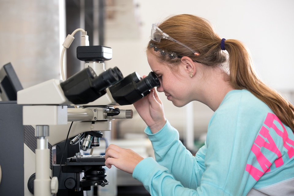 Female BioScience students views a slide under a microscope