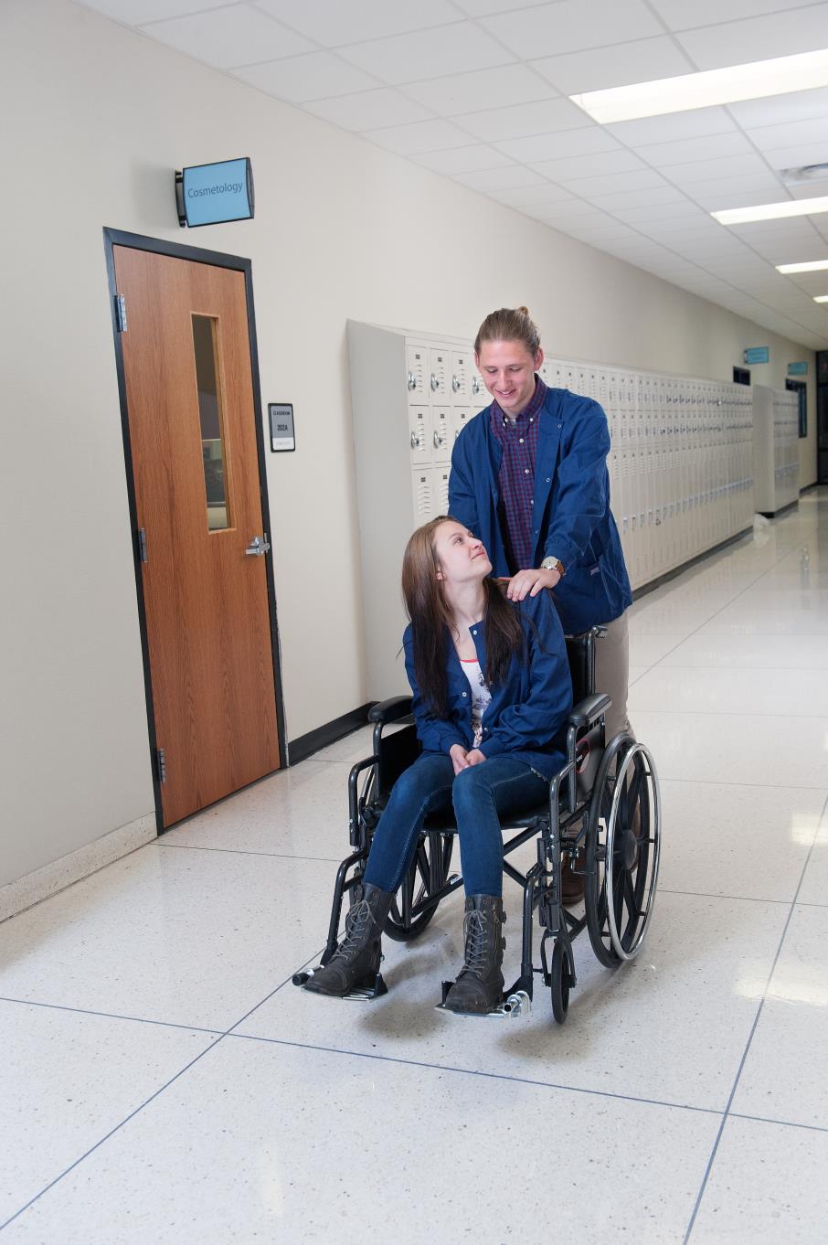 Male Health Foundations student pushes another student in a wheelchair down the hallway