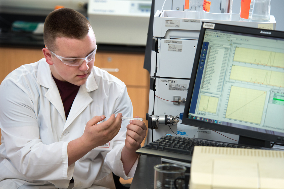 Male BioScience student injects solution into a piece of scientific equipment.