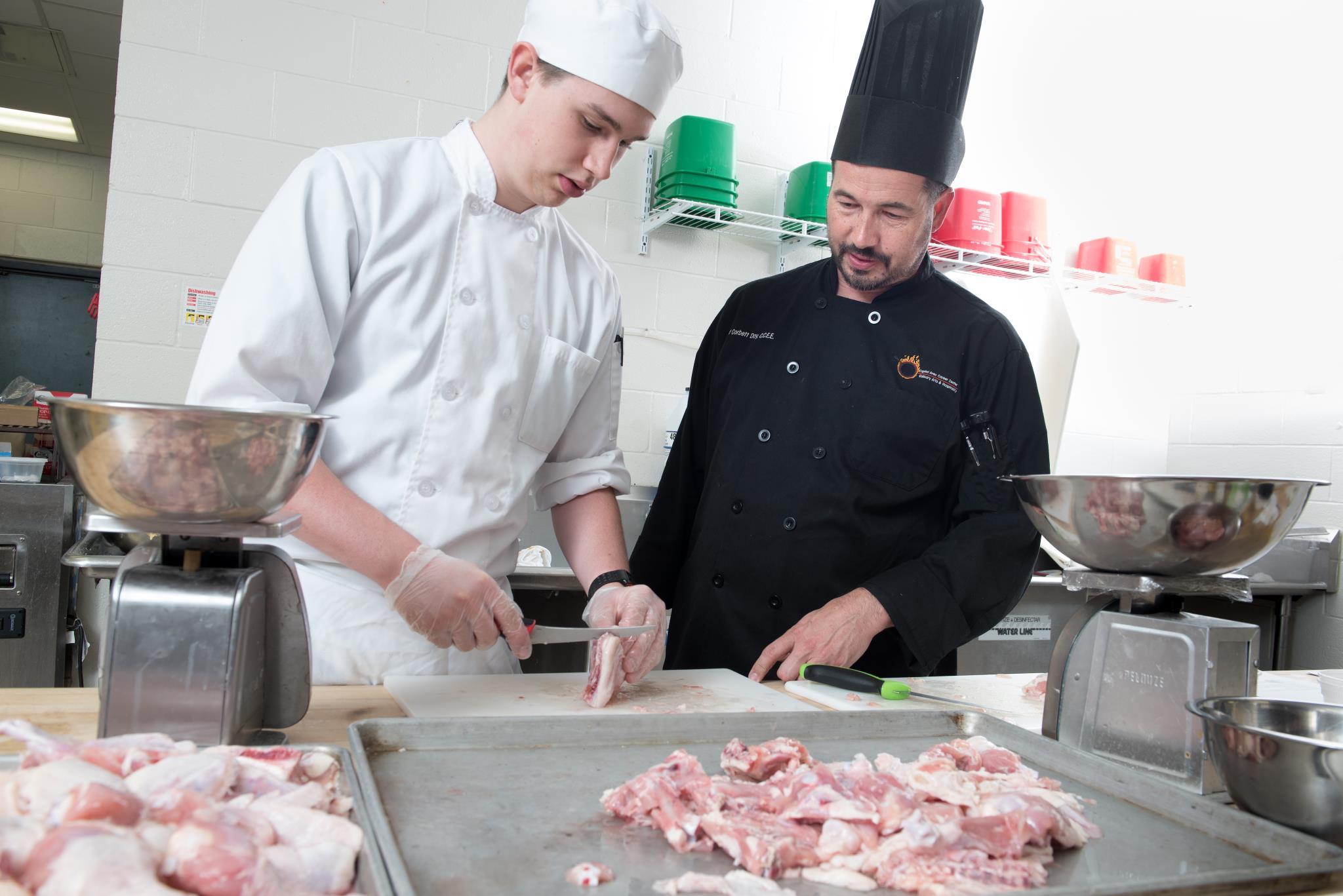 Student learning to cut meat with guidance from instructor in Culinary Arts