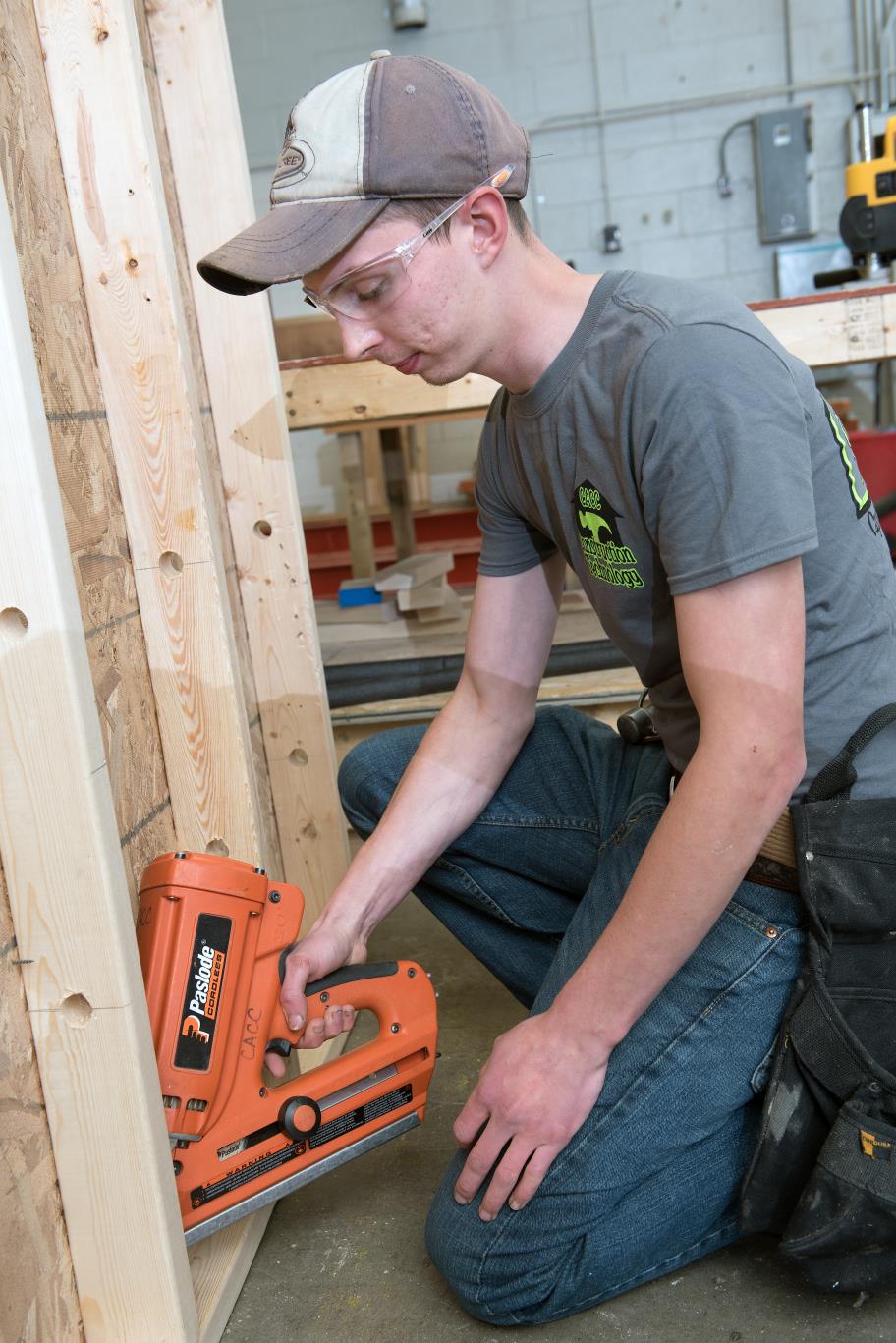Male construction student uses a nailer to adhere two boards together