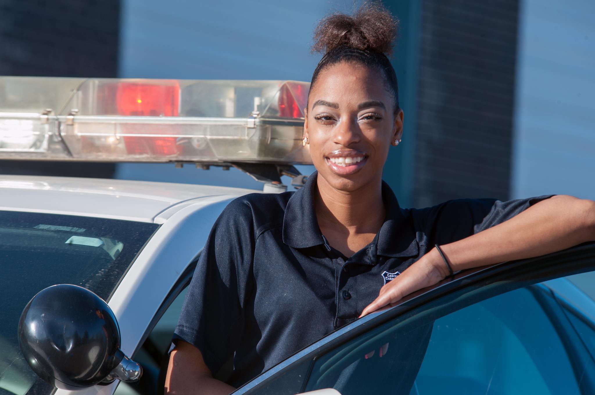 Female Law Enforcement student leans on the door of a patrol car