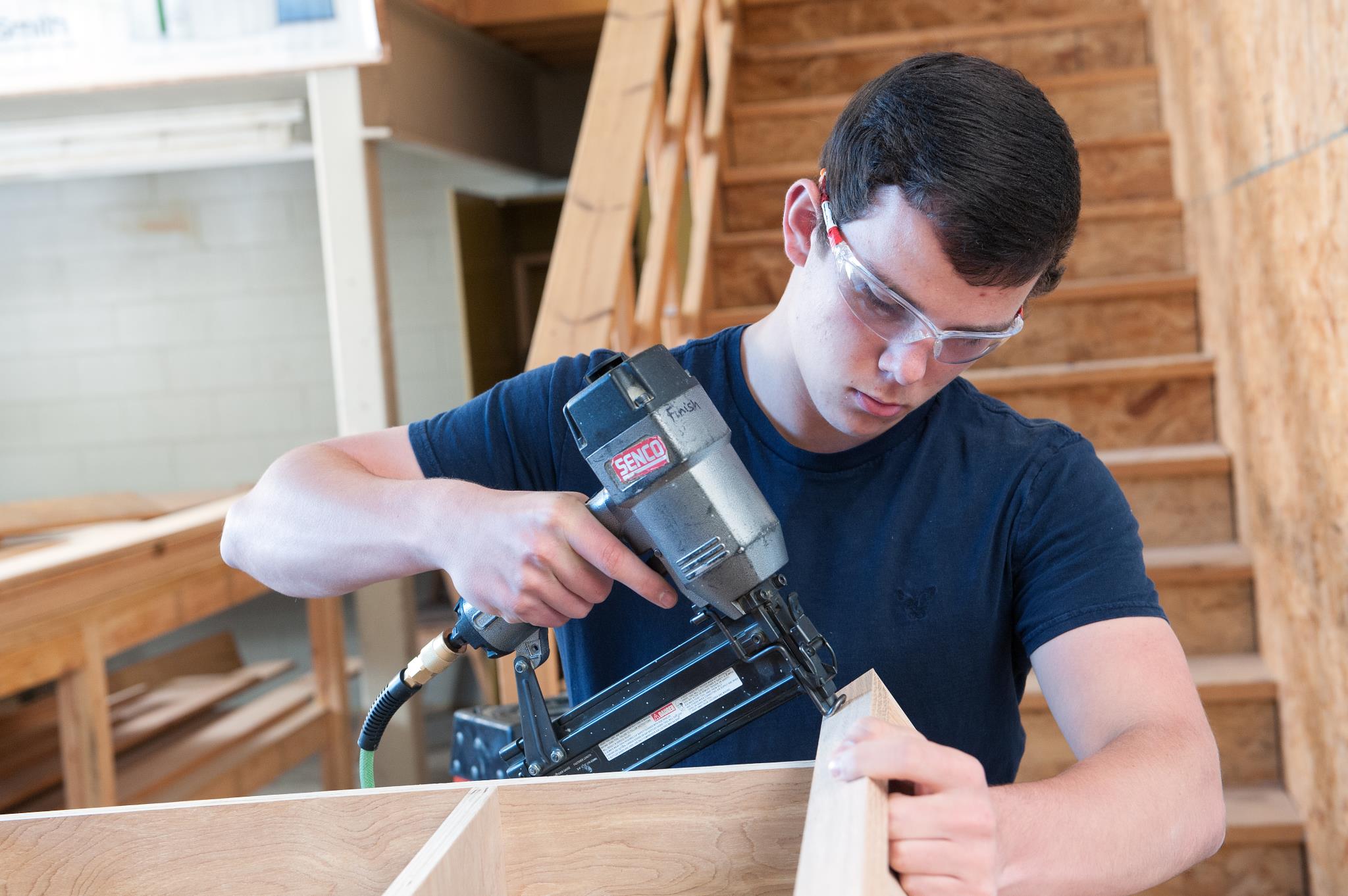 Male construction student uses a drill on a piece of wood