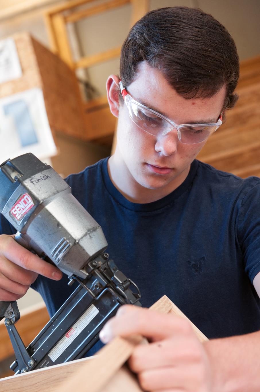 Male construction student uses a drill on a piece of wood