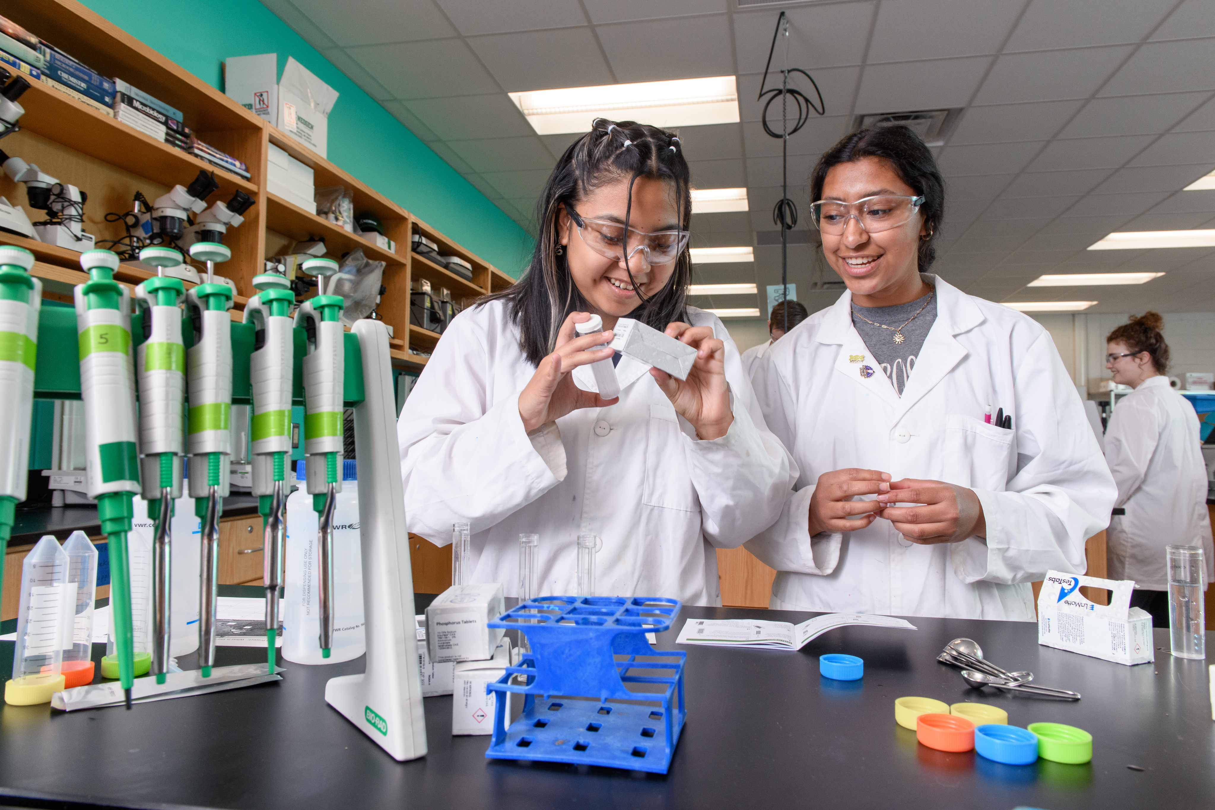 Two BioScience Careers students read the testing kit on a box in the lab.