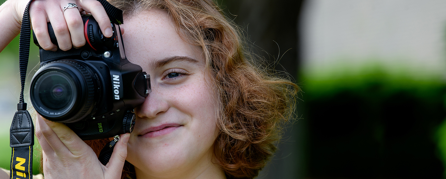 New Media student holds a camera up to her face to take a photo.