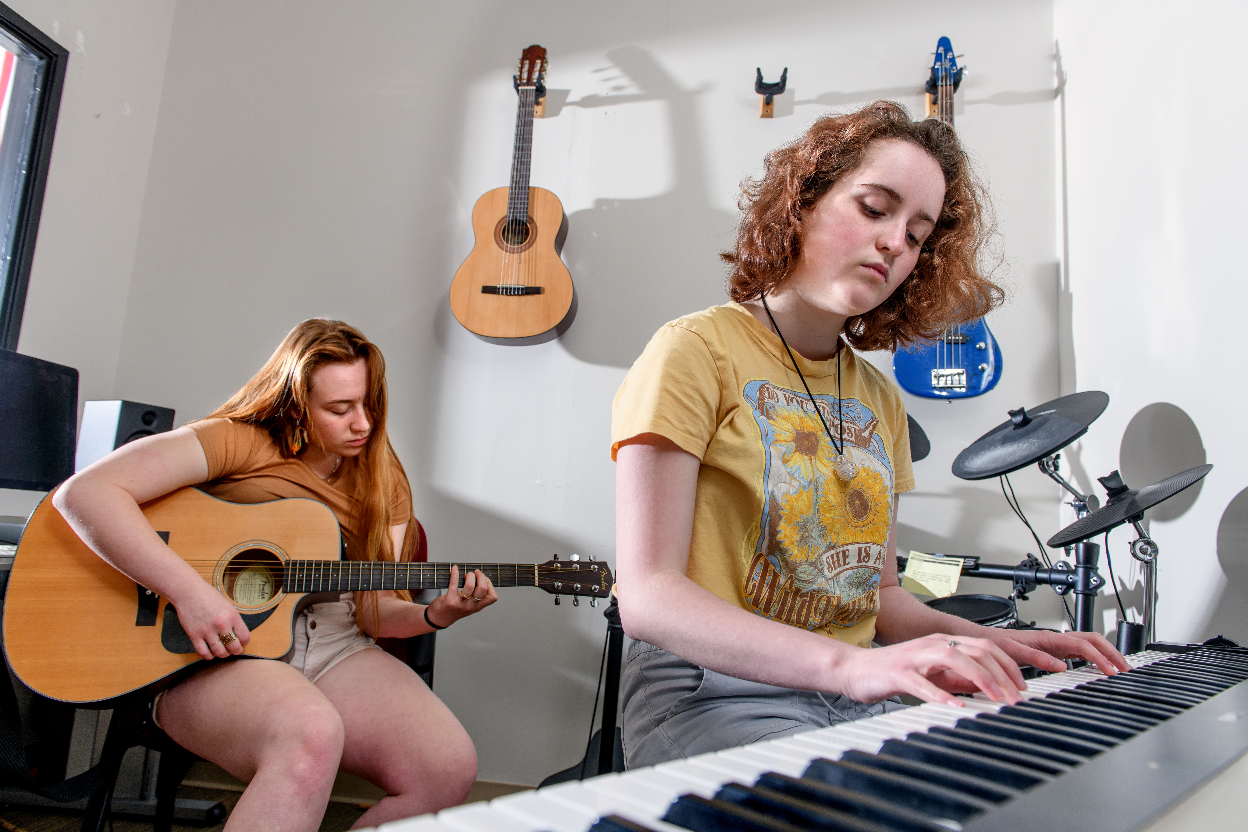 New Media students play the keyboard and guitar in the sound studio.