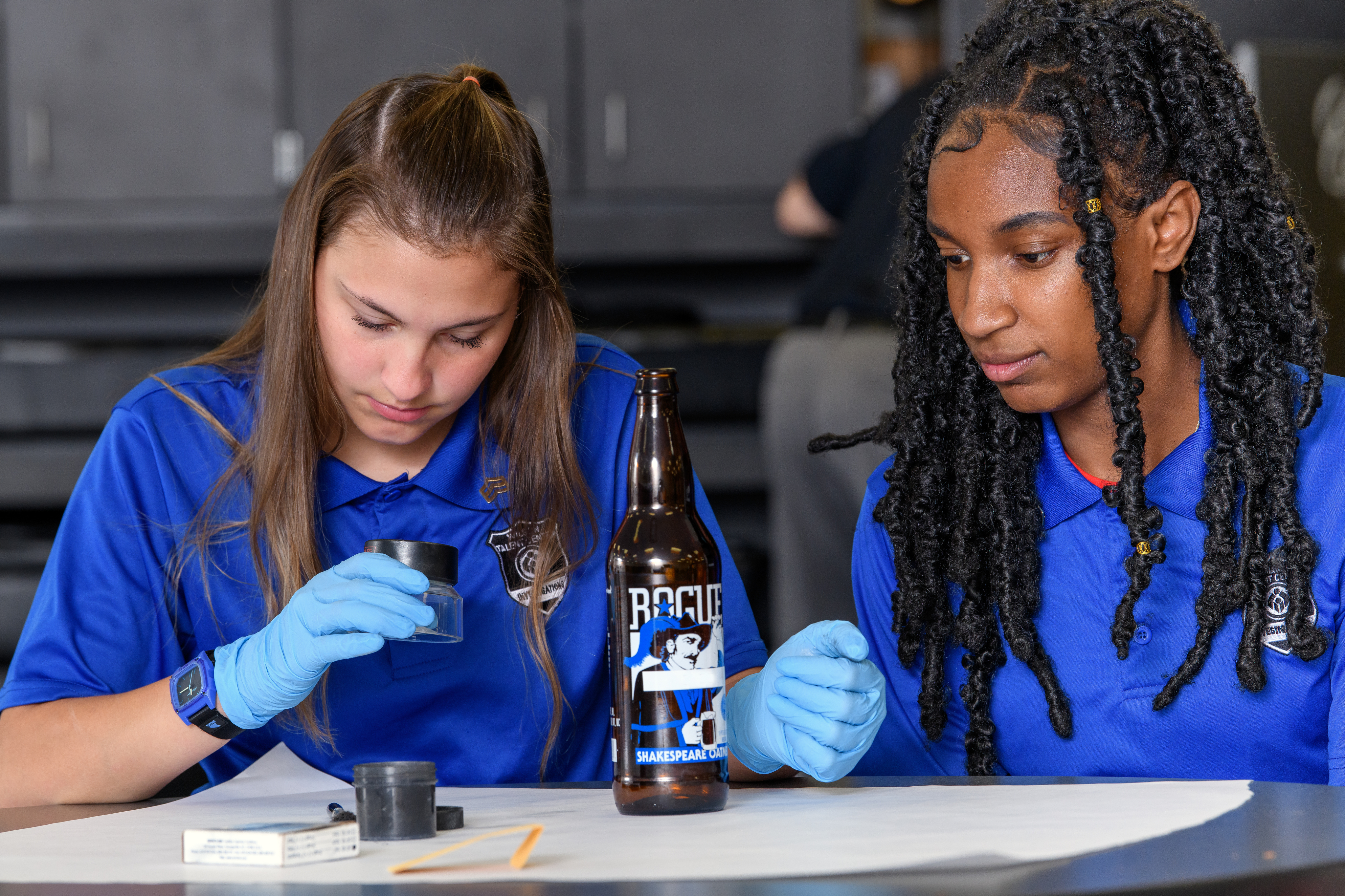 Two female Investigation students dust a bottle for fingerprints.