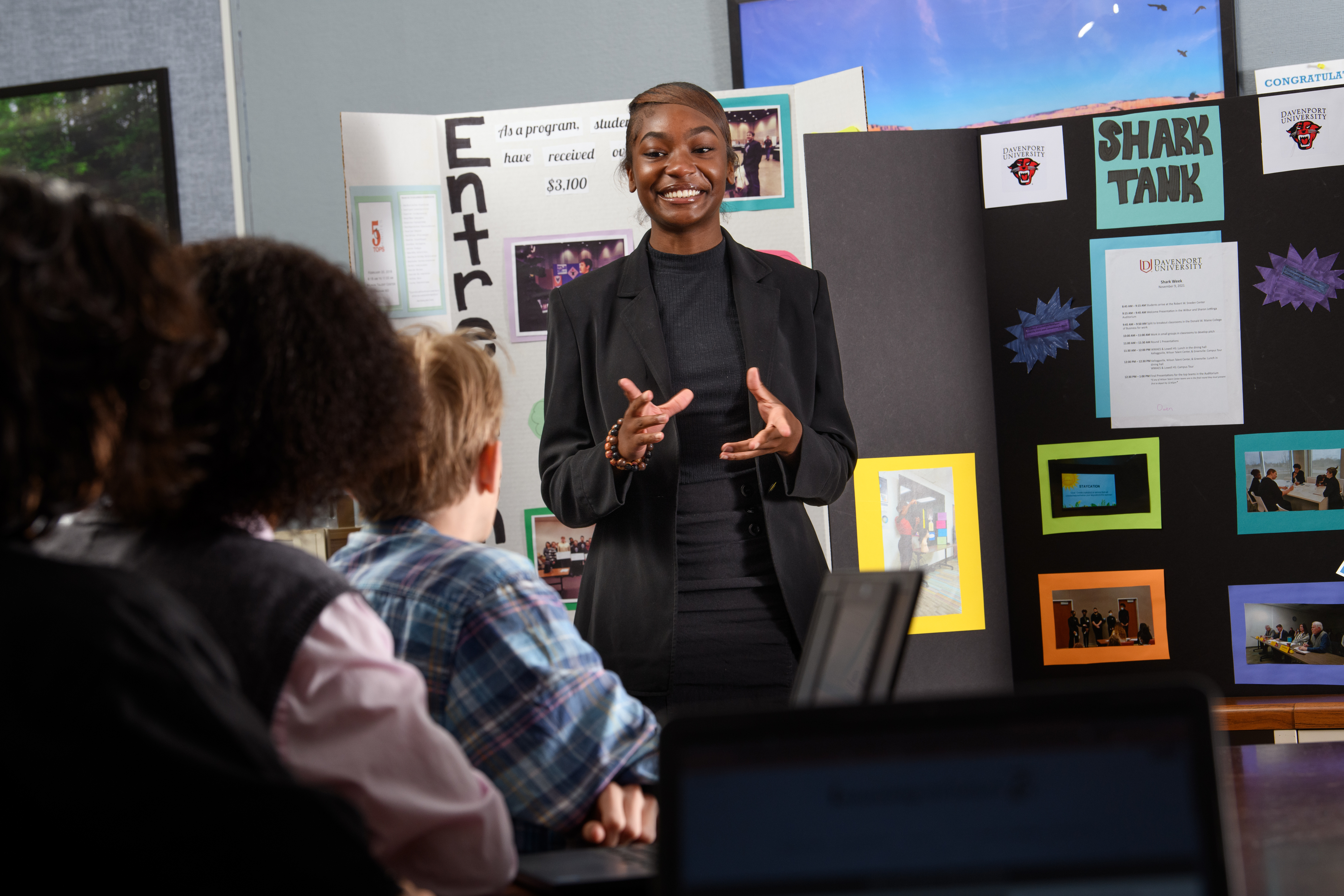 Female Business student stands in front of a presentation board explaining her project to classmates.