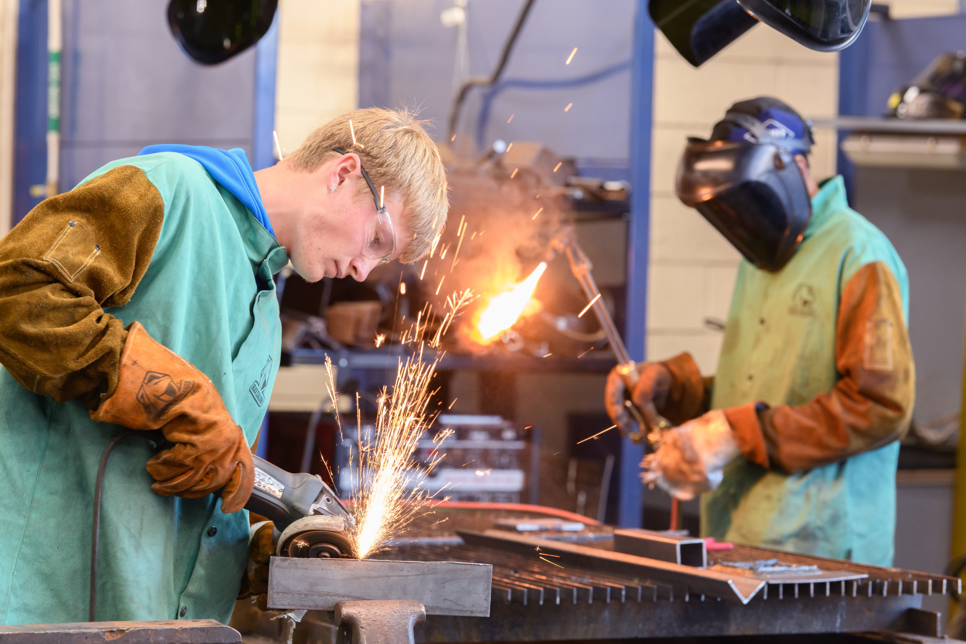 Two welding students work together in the lab cutting and grinding metal.