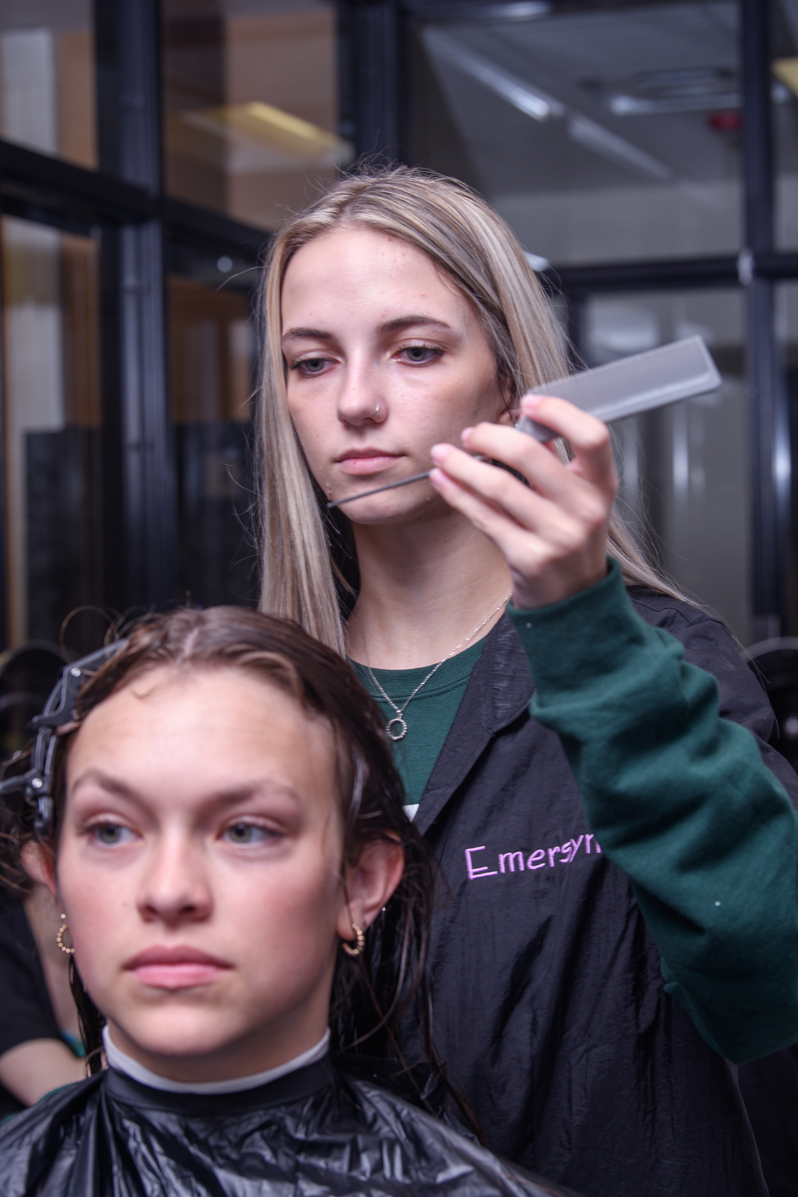 Female Cosmetology student works on sectioning off the hair of another female student.