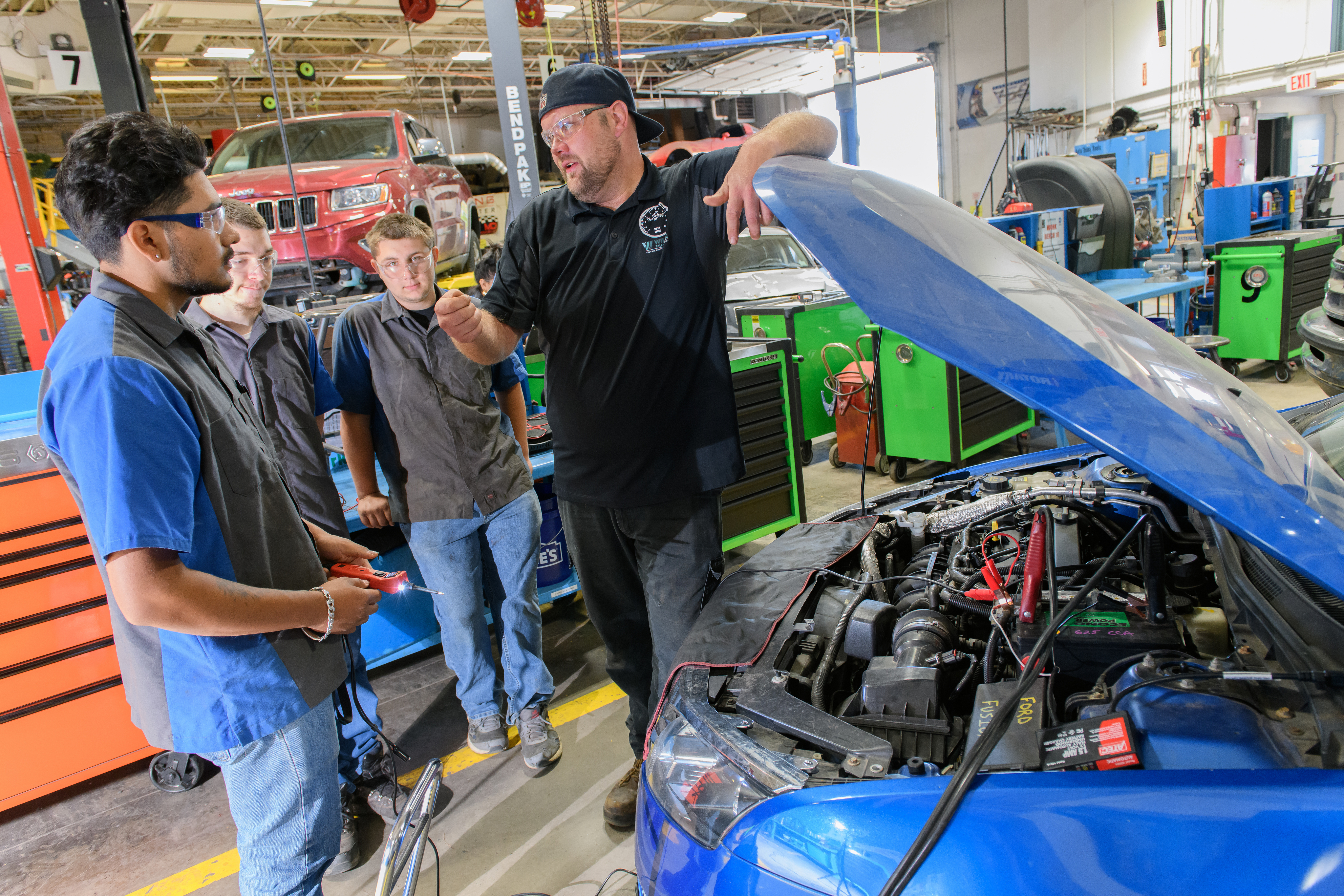 Automotive Technology instructor discusses with 2 students what they need to do to fix the blue car.
