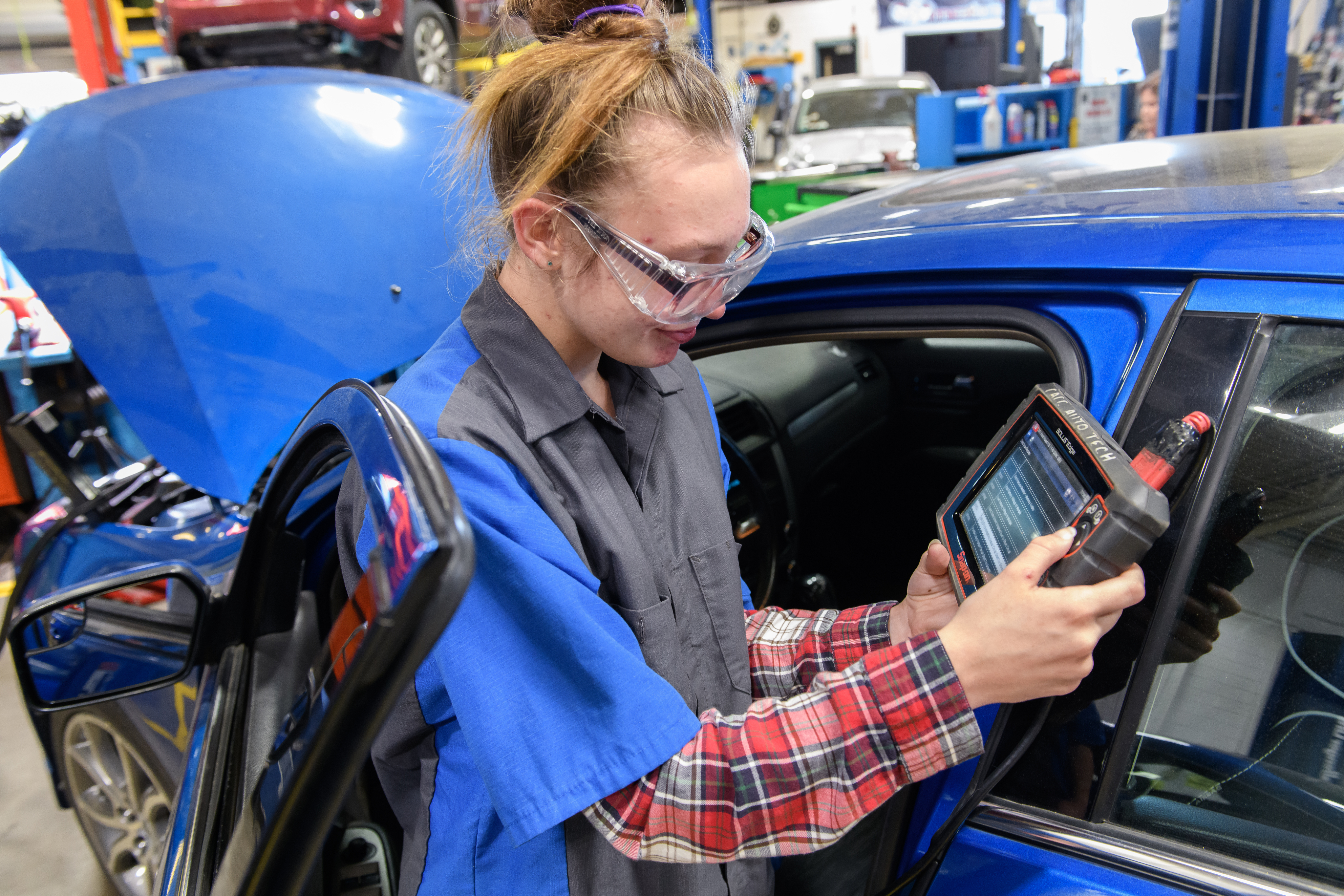 Automotive Technology student holds a computer devise to determine what is wrong with the vehicle.