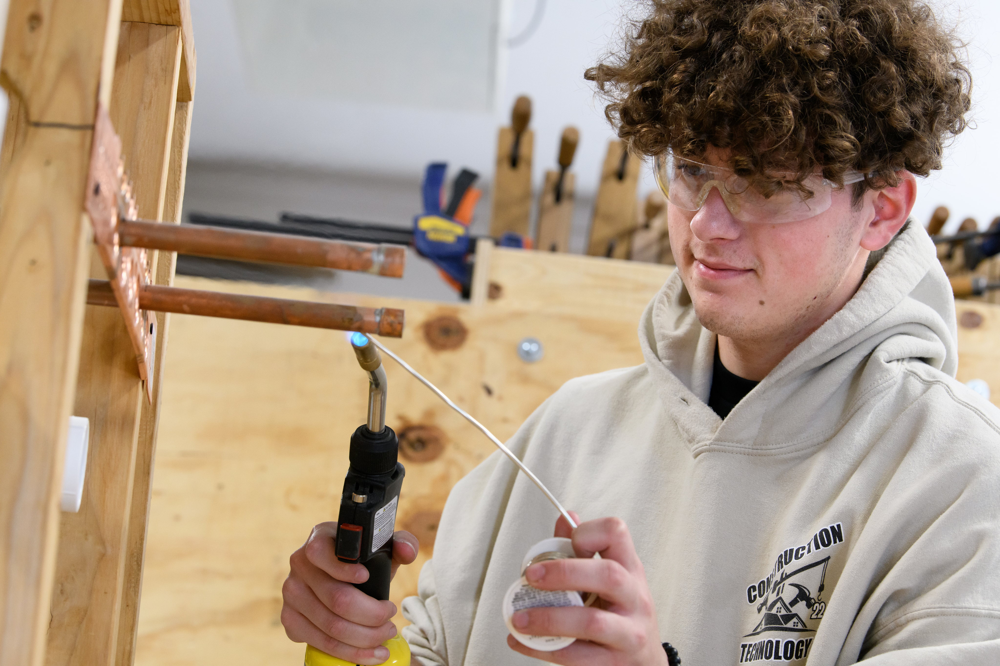 Male construction student uses heat to sodder plumbing materials together.