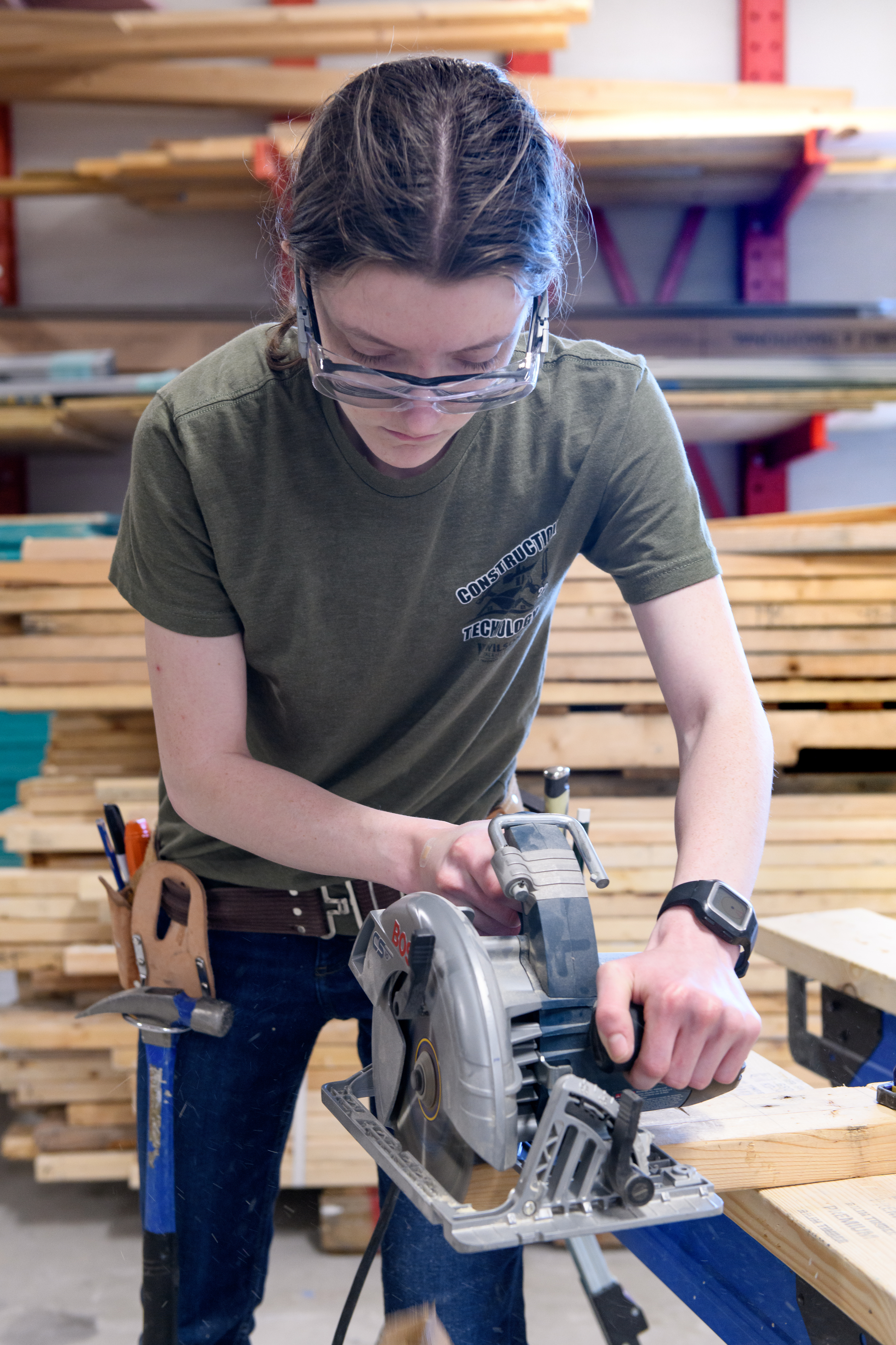 Female construction student uses a handsaw in the construction lab to cut a 2 x 4.