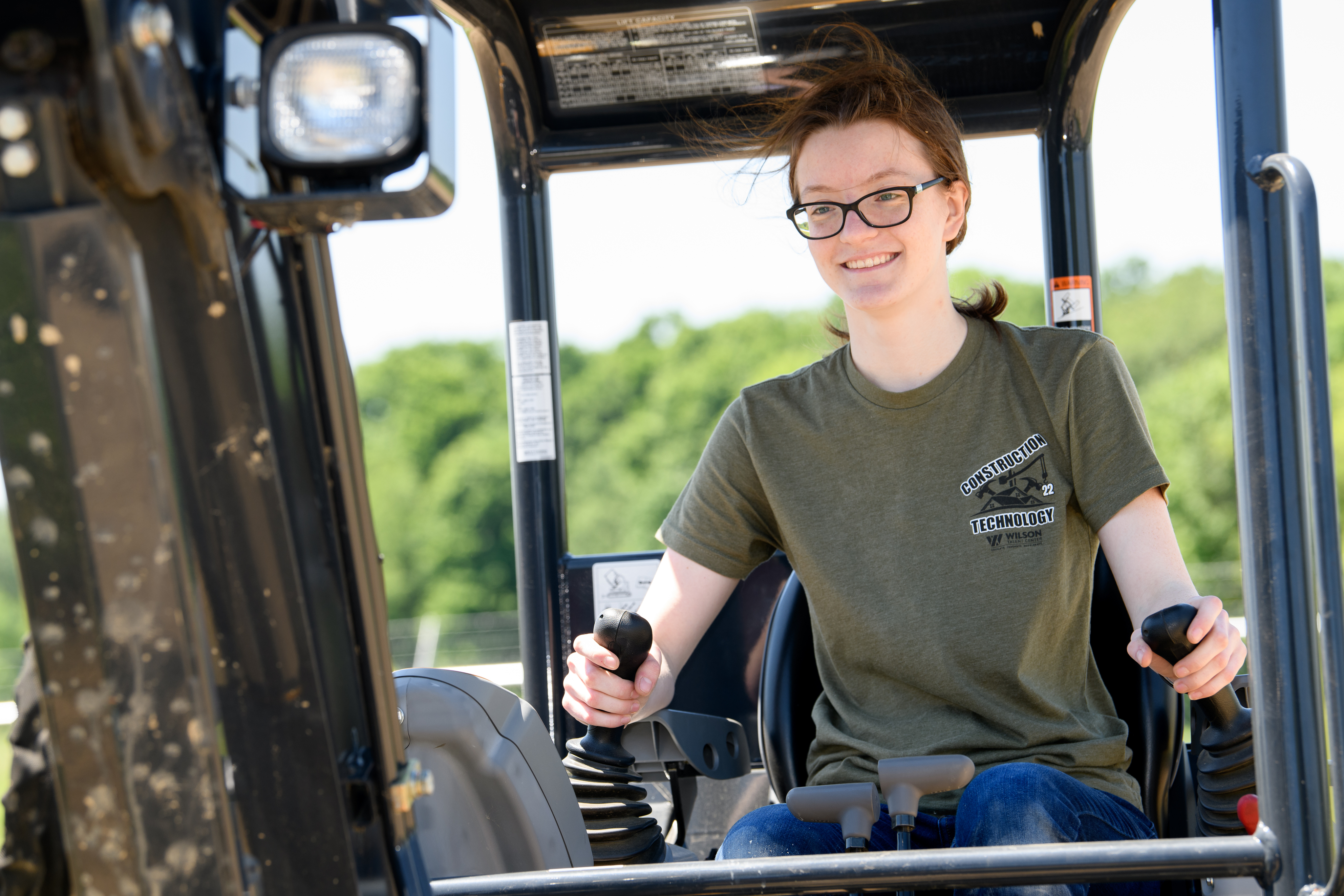Female construction student sits in the cab of the forklift ready to dig up some dirt.