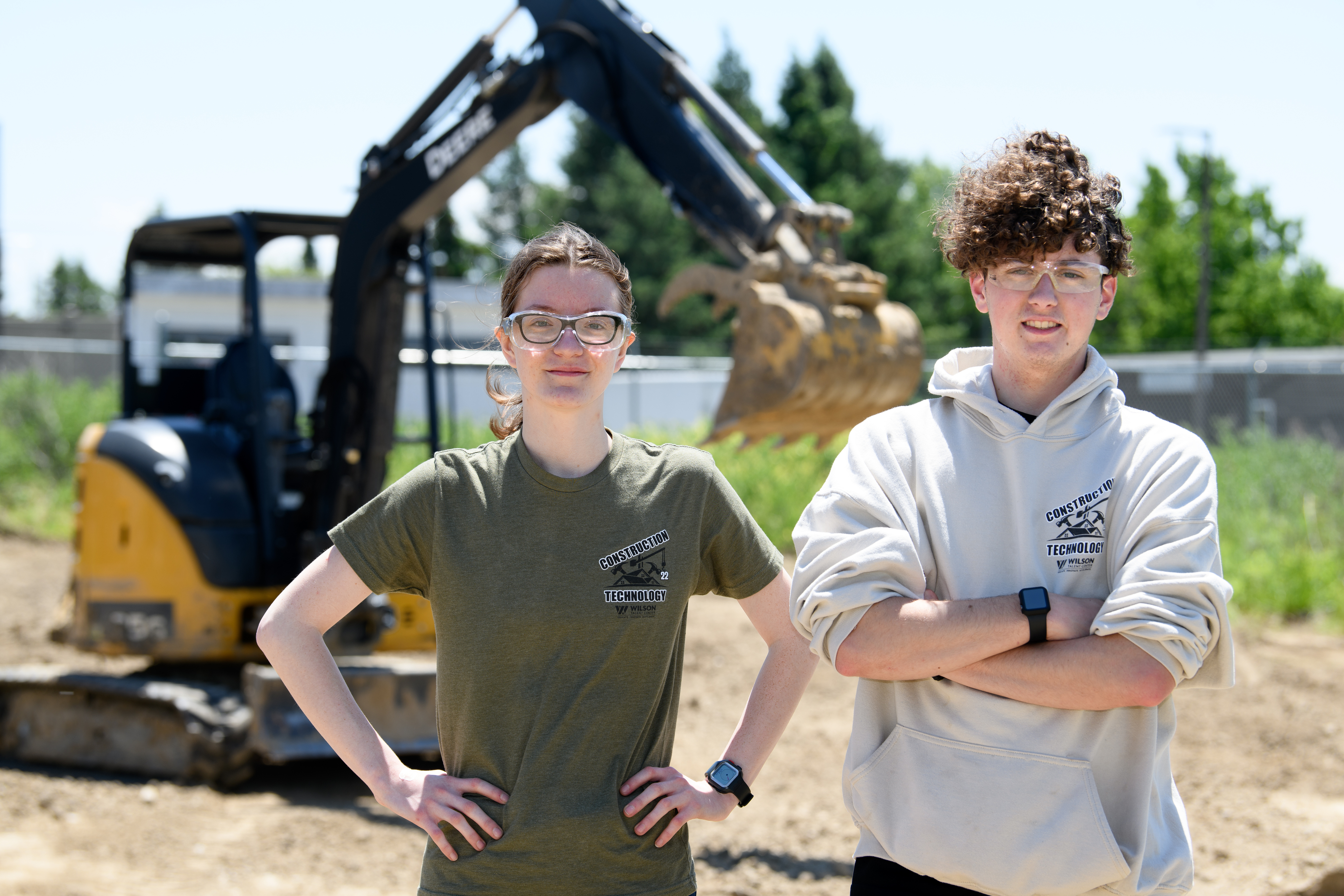 Female and male Construction students stand in the dirt in front of a bulldozer.